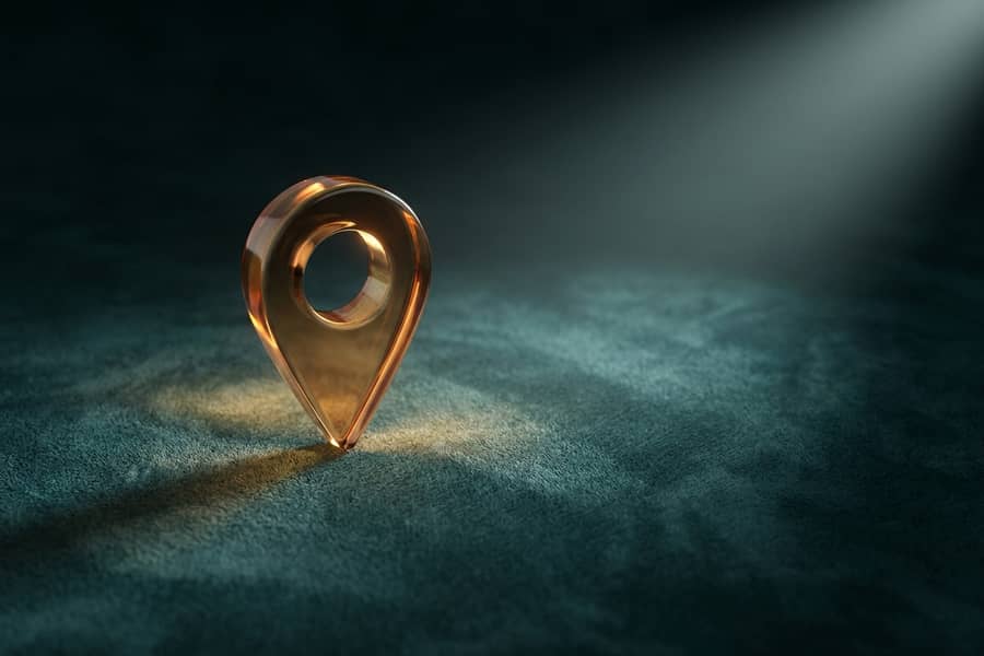 A glass map pin glowing amber on dark teal suede