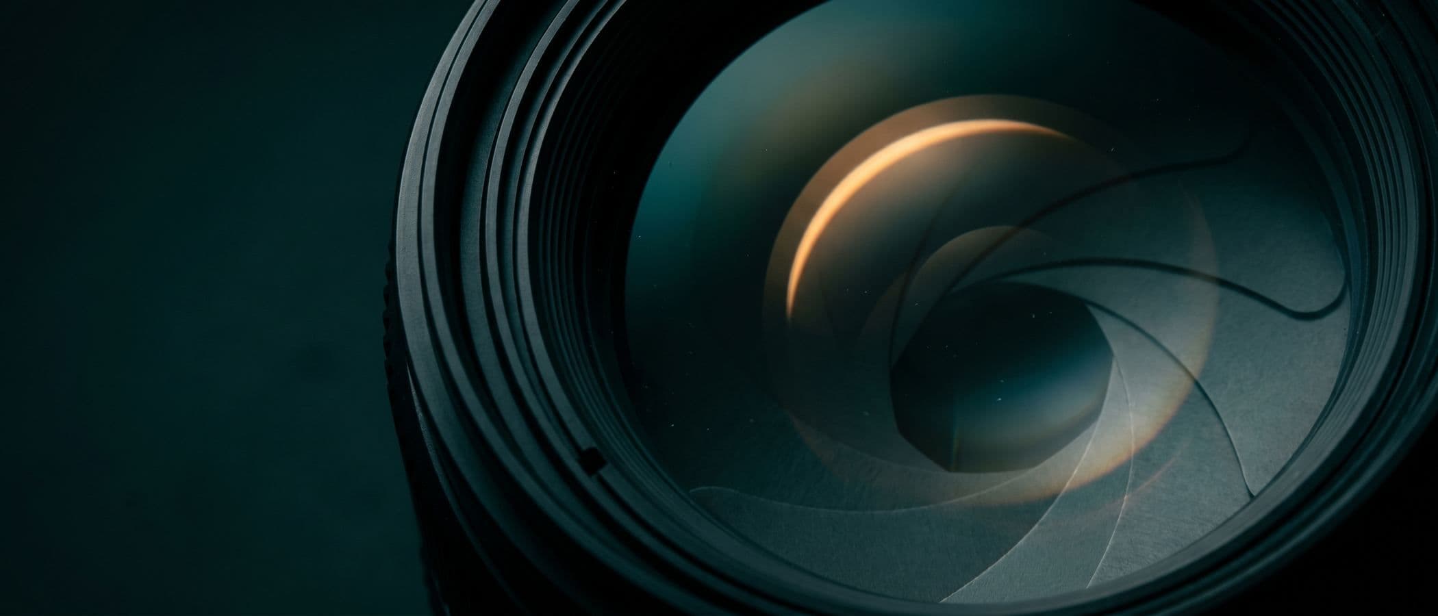 Macro of a camera lens aperture in dark teal with a warm amber light arc