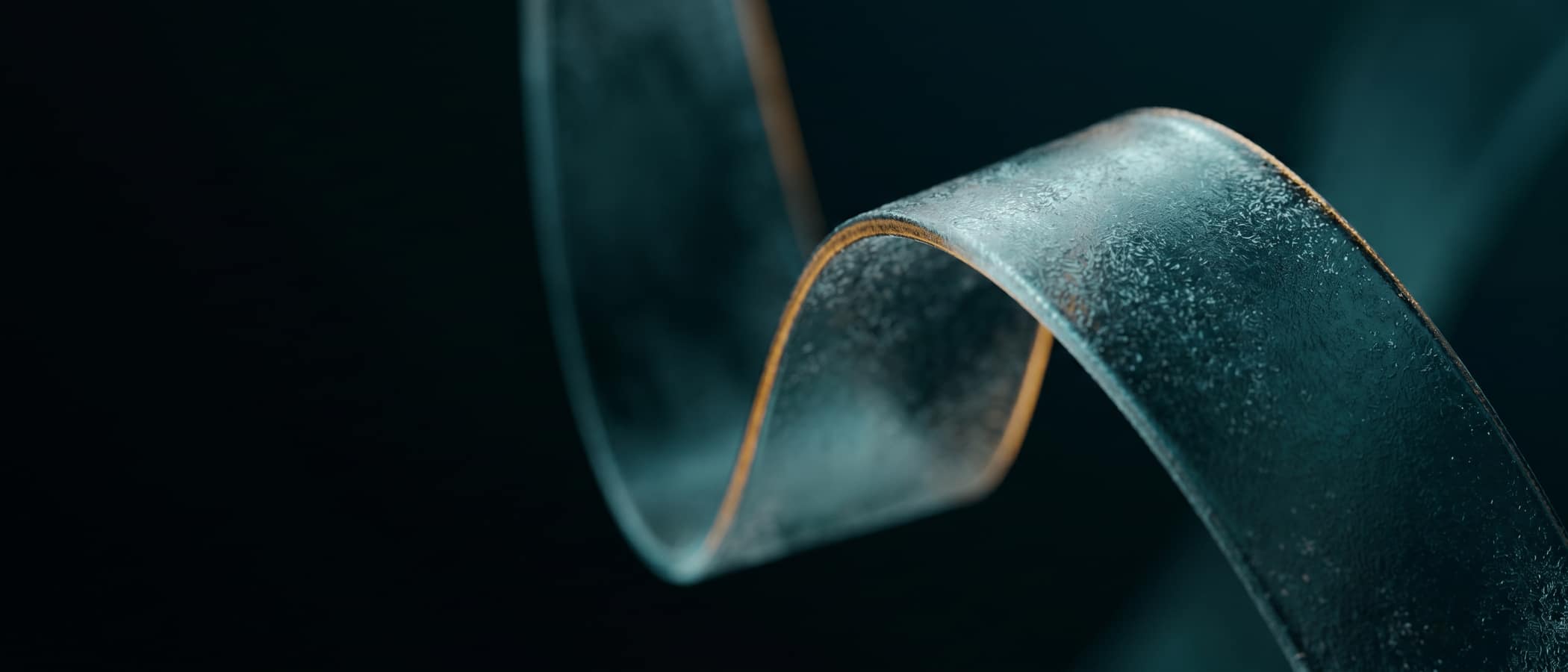 A frosted glass ribbon curving through darkness, one fold catching amber light