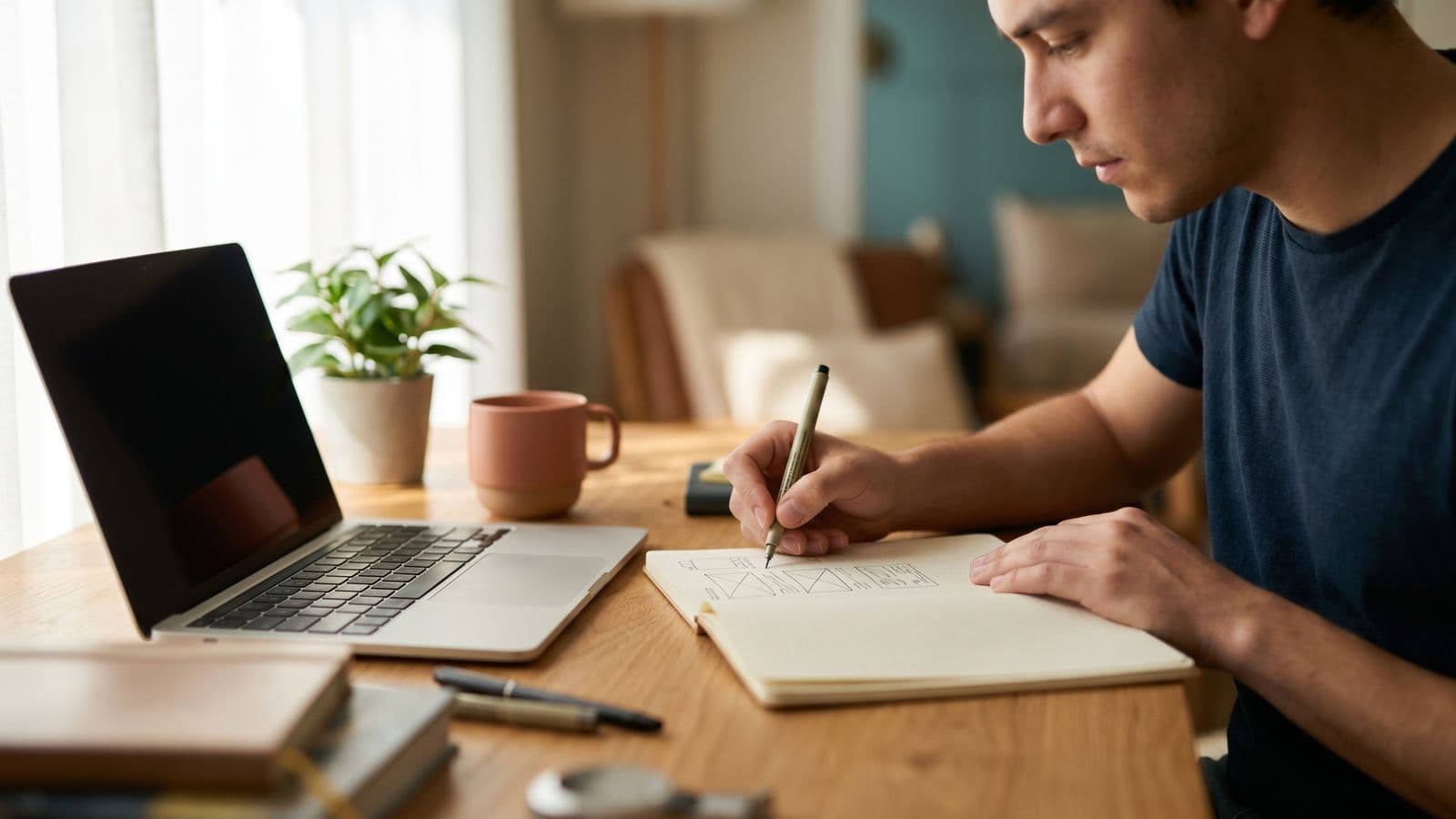Freelance web designer sketching a website wireframe in a notebook beside a laptop